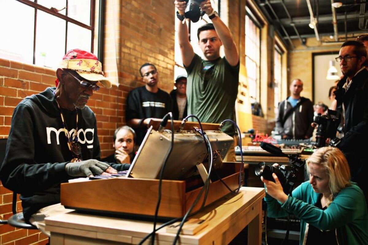 Musician Bernie Worrell, far left, is surrounded by photographers while he plays in the Modular Marketplace at the Boiler Room Lobby during Moogfest in Durham in May 2016.