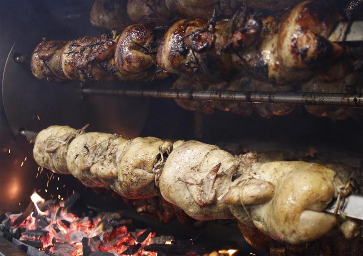 Chicken cooks over wood charcoal briquettes at Alpaca Peruvian Charcoal Chicken. The rotisserie chicken has been marinated overnight in special house seasoning.