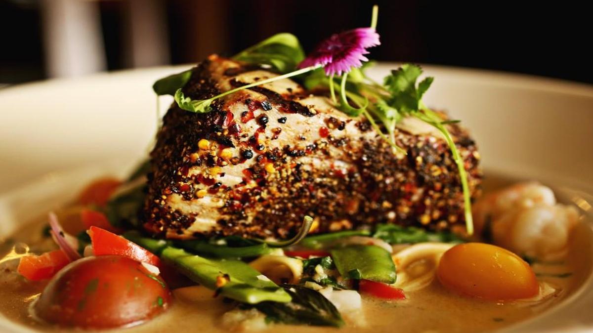 The signature Voodoo Tuna - a thick peppercorn-encrusted filet served over noodles and snap peas in a coconut-shellfish sauce that fairly hums with the complex harmonies of garlic, ginger, cumin, Thai chiles and cilantro at Maximillians Grill and Wine Bar in Cary.