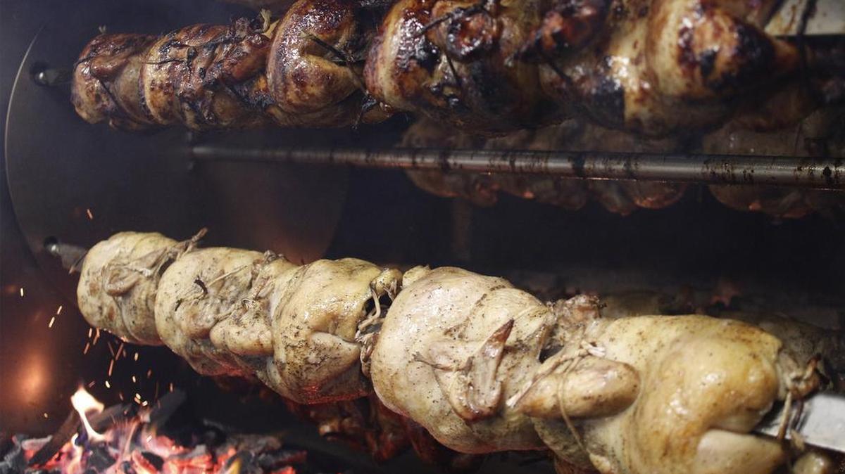 Chicken cooks over wood charcoal briquettes at Alpaca Peruvian Charcoal Chicken. The rotisserie chicken has been marinated overnight in special house seasoning.