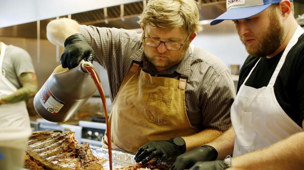 Wyatt Dickson, left, adds his trademark sauce as he and Michael Armstrong pull the meat from freshly smoked pork at Picnic in Durham on Thursday, Sept. 1, 2016. Rather than chopping or slicing the pork, in pursuit of a more satisfying texture, Dickson pulls it from the smoke darkened carcass to produce coarse tatters and shreds. He doesn’t sauce the meat, either, preferring to let people experience its subtly smoky flavor on its own before saucing it to taste with his trademark sauce — which, wouldn’t you know it, is a fusion of Eastern and Western styles.