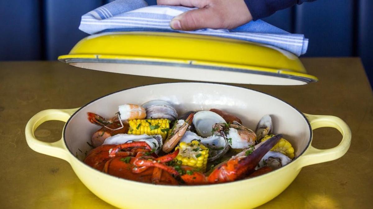 A server lifts the lid on a Saint James 'Steam Pot' with half lobster, shrimp, clams, oysters, andouille, potatoes and corn at Saint James Seafood on Thursday, Mar. 14, 2018, in Durham, NC.