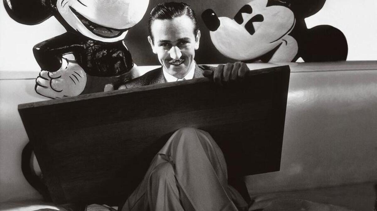 
Walt Disney seated with drawing board on his lap and representations of his creations Mickey and Minnie Mouse, ca. October 1933. 
