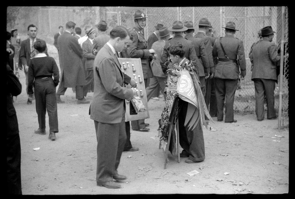 A boy sells pennants as NC Highway Patrol troopers file into the stadium before the sold-out Duke-Carolina game played in Durham, NC in 1939.