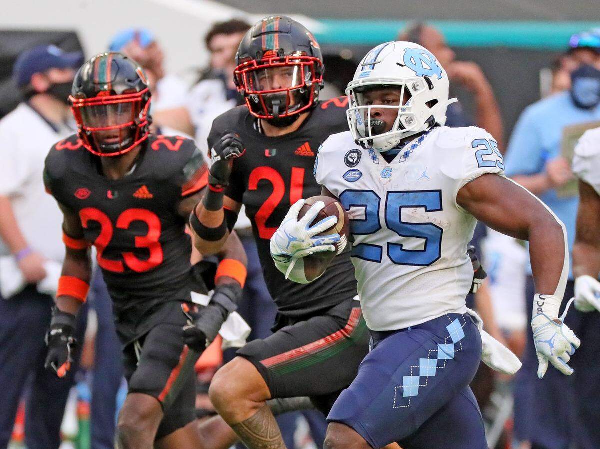 North Carolina Tar Heels running back Javonte Williams (25) runs the ball in the second quarter as University of Miami cornerback Te’Cory Couch (23) and Bubba Bolden (21) give chase at Hard Rock Stadium In Miami Gardens, Florida, Saturday, December 12, 2020.
