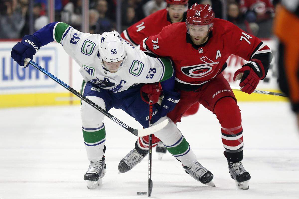 Vancouver Canucks center Bo Horvat (53) and Carolina Hurricanes defenseman Jaccob Slavin (74) vie for the puck during the first period of an NHL hockey game in Raleigh, N.C., Sunday, Feb. 2, 2020. (AP Photo/Gerry Broome)