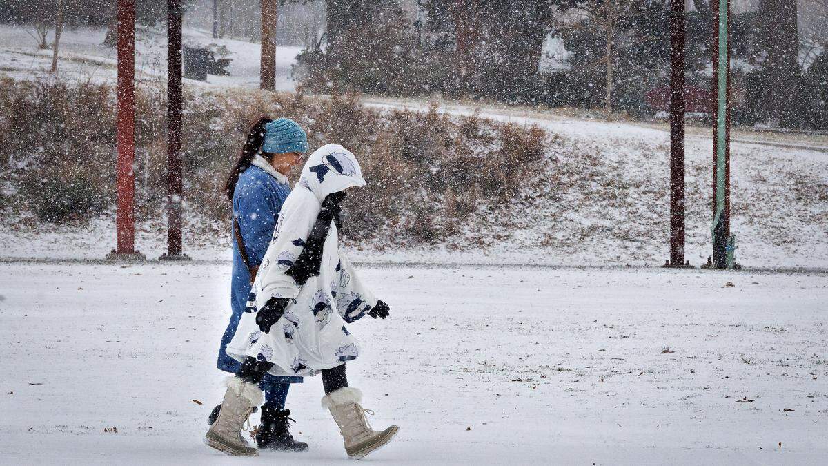 People walk along Foster Street as snow falls on Saturday, Jan. 31, 2026, in Durham, N.C.
