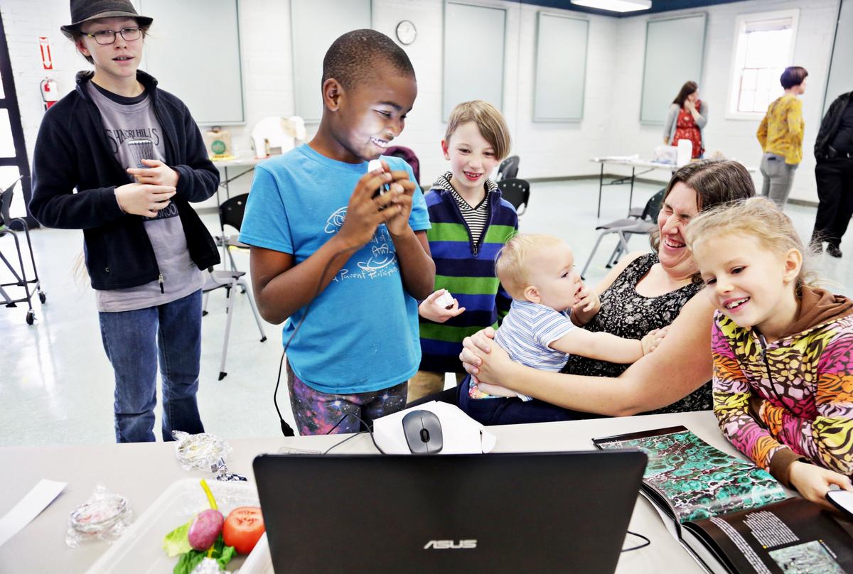 Students of varying ages gather around 9-year-old Ambrose Everett as they use a digital microscope to explore nearby items, including themselves, during the weekly Homeschool Explorers meeting for students and parents at Method Community Center in Raleigh on Tuesday, Nov. 27, 2018.