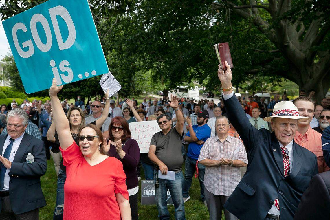 Retired pastor Dan Patrick Goldsboro, N.C., right, holds up his bible, and Lisa Ragan of Sanford, N.C., left, react during a Return America rally, calling on Governor Cooper to rescind his executive order prohibiting churches from holding indoor worship services on Thursday, May 14, 2020 on the Legislative grounds in Raleigh, N.C.