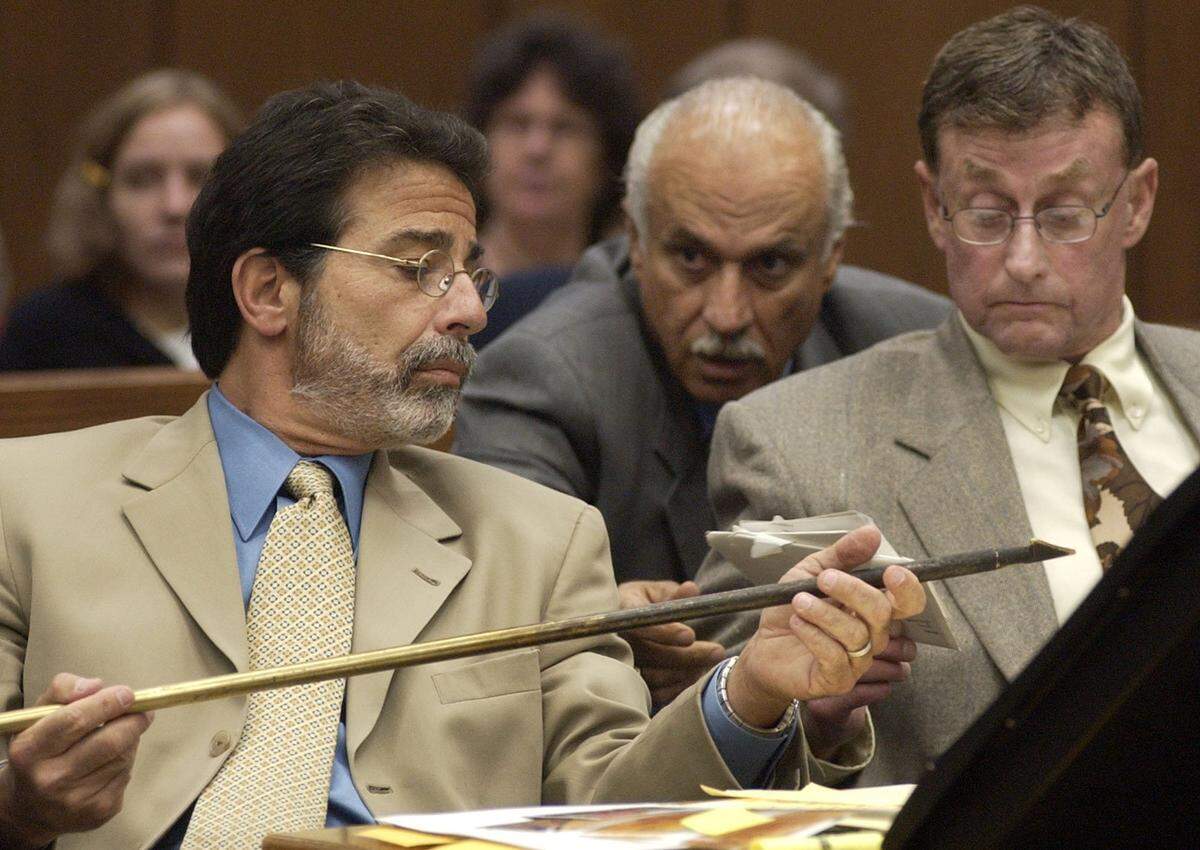 Defense attorney David Rudolf, left, examines a fireplace blow poker which District Attorney Jim Hardin entered into evidence Tuesday, July 15, 2003, during the Michael Peterson murder trial in Durham, N.C. Peterson, right, and defense investigator Ron Guerette, at center, rear, ready to hand Rudolf some photos.