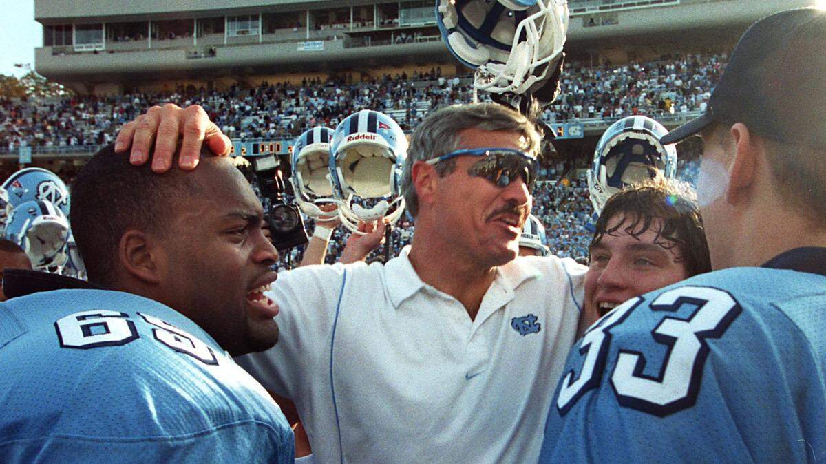 UNC head football coach Carl Torbush is surrounded by his players after being briefly lifted aloft by them. From left Kareem Ellis and (65) and Allen Mogridge (75) and Derrick DePriest . The Tar Heels defeated the Duke Blue Devils 38-0 in Kenan Stadium in 1999.