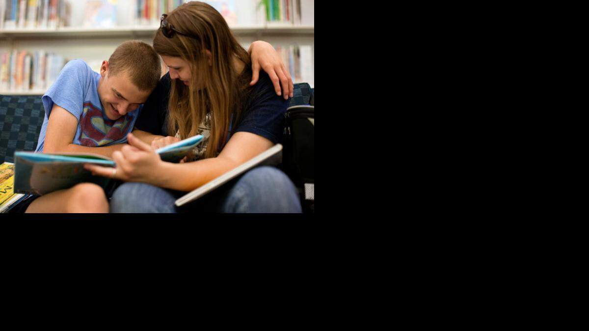 Mason Leonard, 14, reads with Brittney Luchene, his lead therapist, recently at the Eva Perry Regional Library in Cary. Luchene takes Leonard out into the community in the afternoons, using the outings as learning opportunities.
