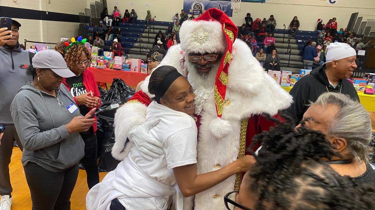 Jeanette Scott, a volunteer with Lost Sheep Outreach Ministries, gets a hug from Santa at the 27th annual toy giveaway Saturday at St. Augustine’s University