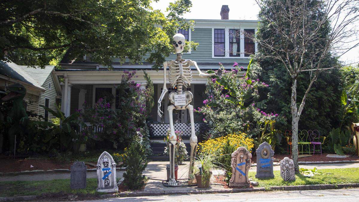 A 13-foot skeleton telling people to vaccinate or die and mock tombstones are on display at the home of Jesse Jones in Raleigh’s Oakwood neighborhood.