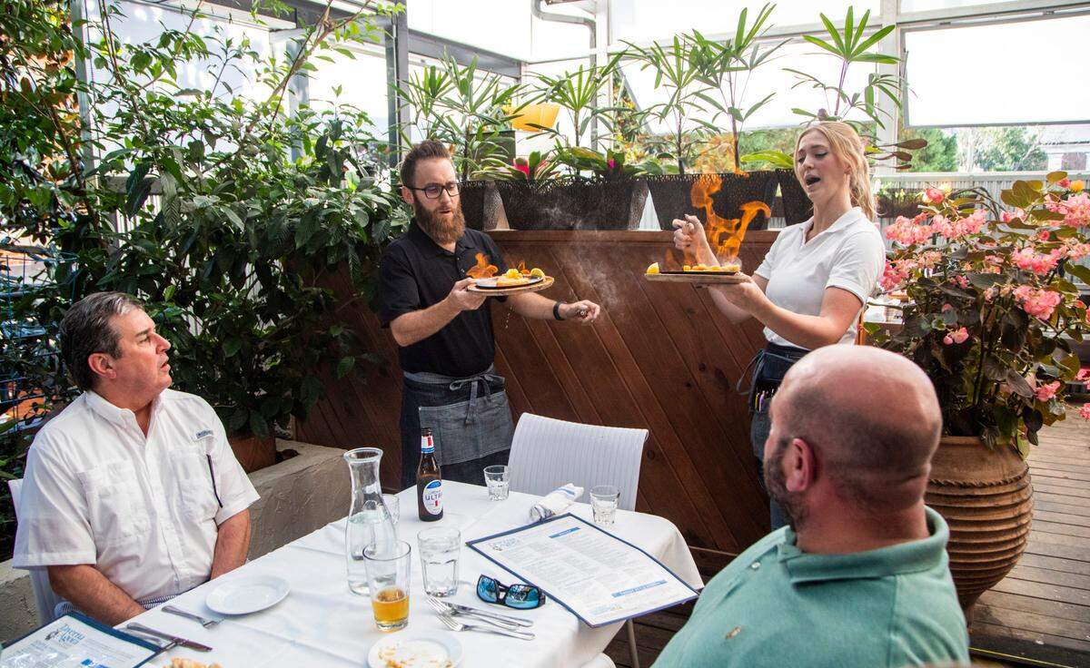 Food runner Lee Baine and server Charlotte Jones bring saganaki flaming cheese dishes to diners Wednesday, June 16, 2021 at Taverna Agora Greek Kitchen & Bar in Raleigh. Many restaurants say business is starting to return to normal as coronavirus restrictions have lifted but hiring remains a challenge.
