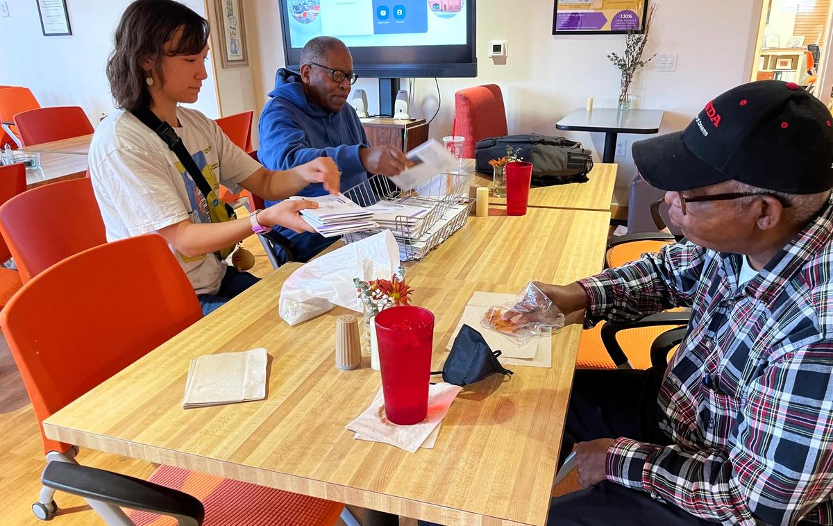 A Club Nova colleague helps staff member M. Ren-Wen Huang prepare copies of the monthly Stargazer Gazette newsletter to go in the mail, while another club colleague grabs a quick bite to eat on Monday, Nov. 11, 2024, in Carrboro.