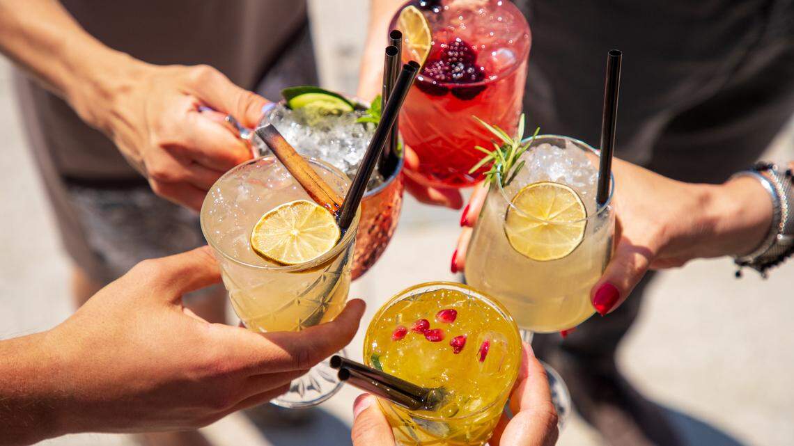 Five exotic cocktails on ice in hands joined in celebratory toast
