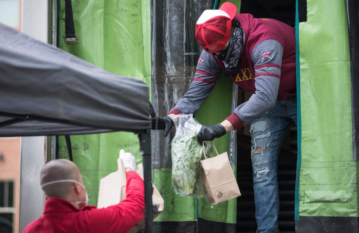 Fernando Suarez, right, hands a food order to Tally Lassiter to be taken to a customer’s car in East Main Square in Carrboro, N.C. on Tuesday, March 31, 2020. The Carrboro United Local Food Hub, which coordinates distribution of family style meals and goods from local restaurants, is an effort to safely feed people while reinvigorating the local economy for the duration of the COVID-19 outbreak.