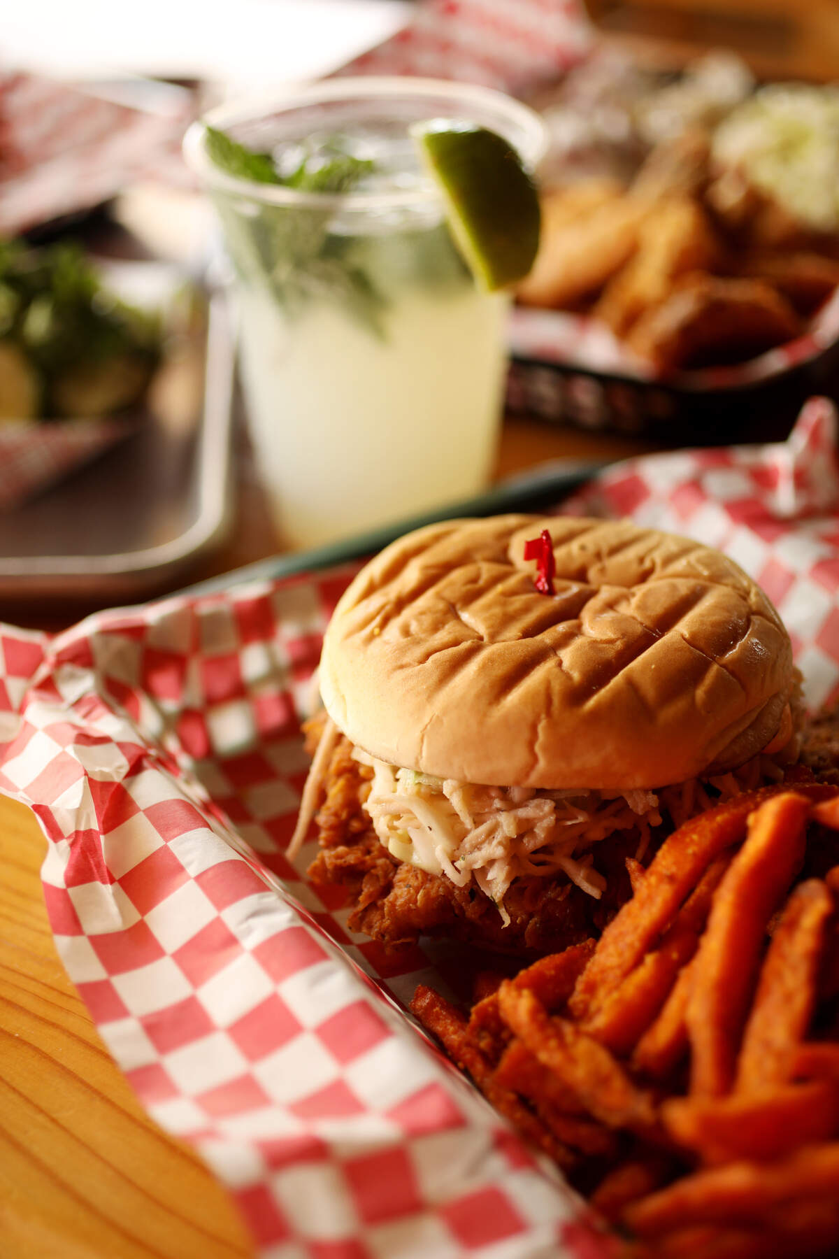 The Deeluxe chicken sandwich at Deeluxe Chicken in Durham is made up of buttermilk fried chicken breast with apple-celery root slaw and sambal mayo. It is served here with a side of shoestring sweet potato fries with chili spice and a mojito.