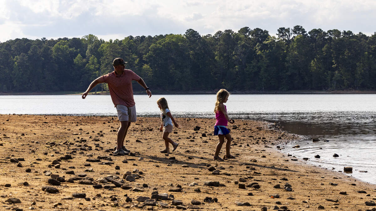 Scott Beasley and his daughters, Virginia Beasley, 3, center, and Ada Beasley, 5, right, toss rocks into Falls Lake from the receded shoreline at Forest Ridge Park in Raleigh on Thursday, June 25, 2026. Raleigh is 18.59 inches below its average rainfall since August 2025, and Falls Lake, Raleigh's primary water source, is 5 feet below its target level. As of mid-June, Durham was about 10 to 12 inches below normal rainfall since the start of the year.