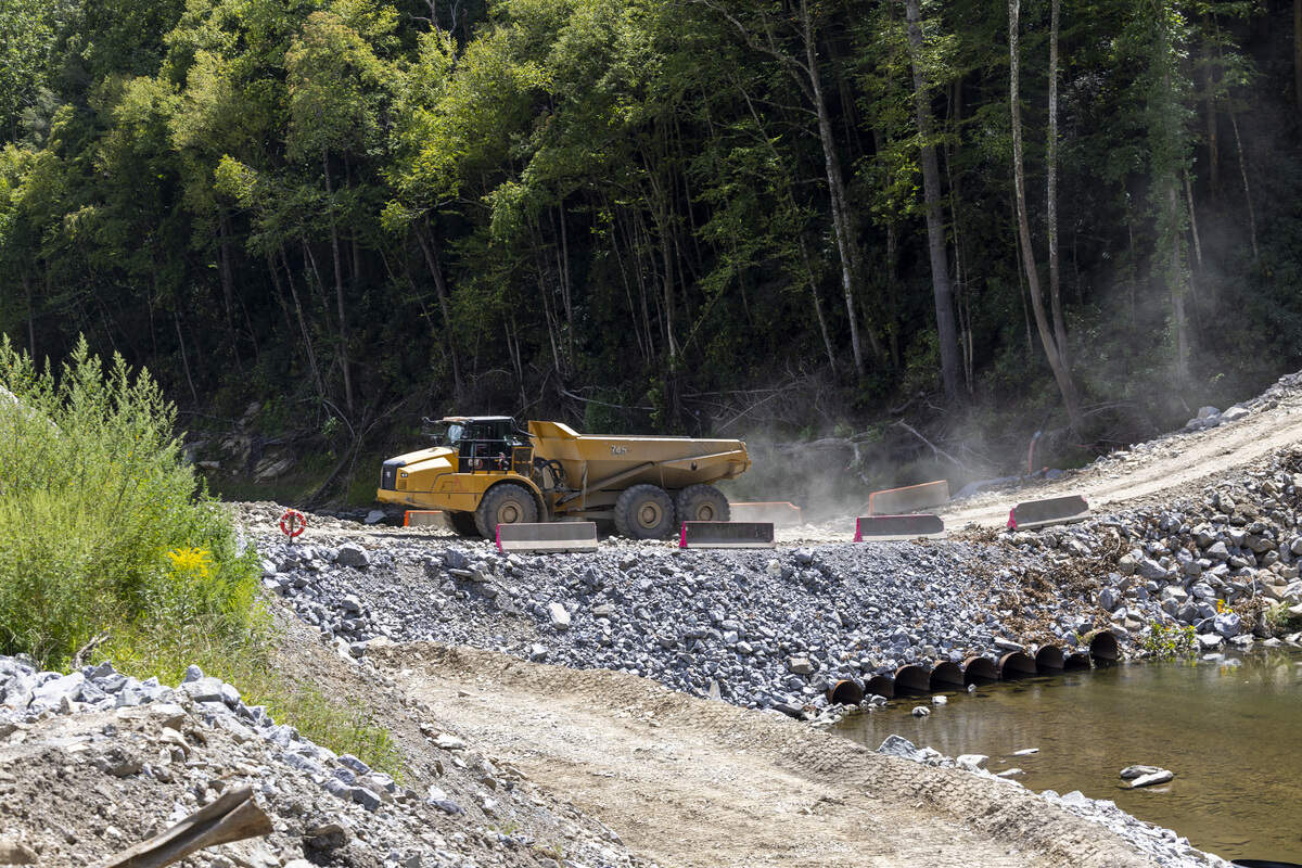 Trucks carry rock across a temporary causeway over the Pigeon River on Thursday. This causeway will be replaced by temporary bridges connecting the Interstate 40 construction site with a quarry being developed in Pisgah National Forest.