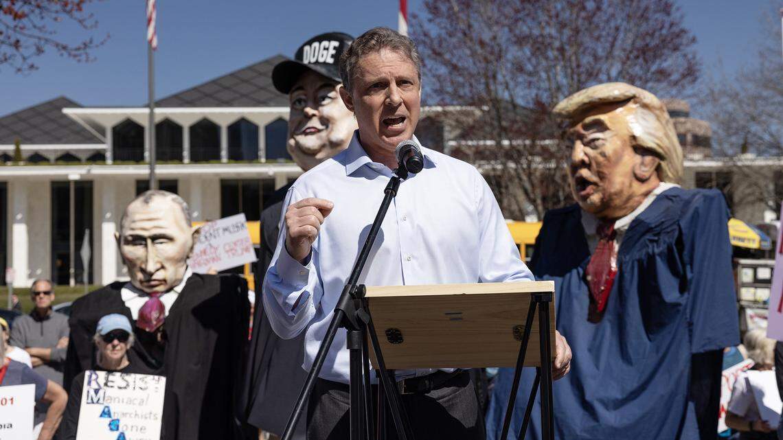Hampton Dellinger, the former U.S. special counsel who was recently fired by President Donald Trump, speaks to protesters opposed to cuts and actions by the Department of Government Efficiency and Elon Musk at a rally outside of the N.C. General Assembly on Wednesday, March 12, 2025. Behind Dellinger are huge puppets of Russian President Vladimir Putin, Musk and Trump.
