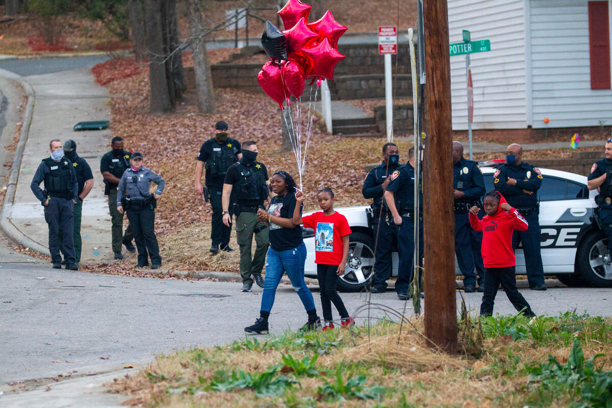 Mourners walk past law enforcement officers prior to a balloon release Thursday, Dec. 16, 2021 in Durham at the site of a Monday morning shooting that left two teenagers dead and four other children injured.