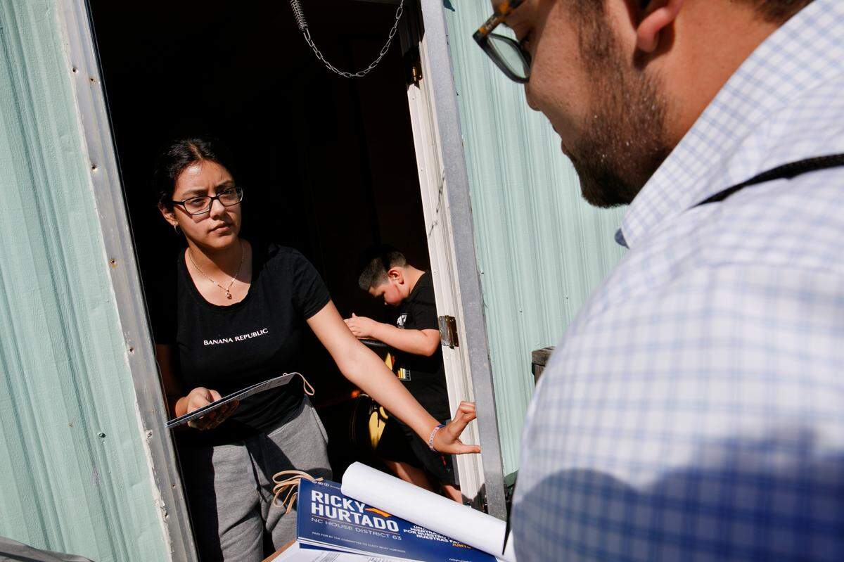 Evelyn Lara, 19, with her brother Iker, 7, opens the door as Ricky Hurtado, a Democratic candidate for the North Carolina state house, canvasses voters in a largely Latino trailer community, in Burlington, N.C., Sunday, March 8, 2020.
