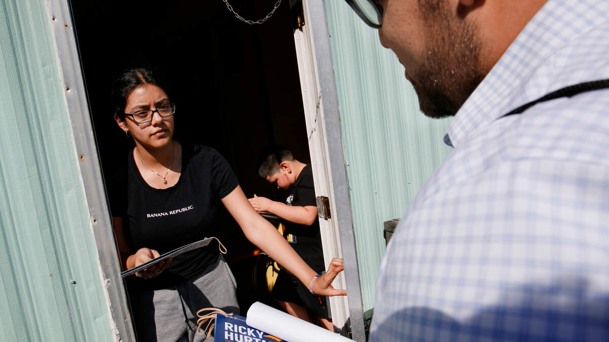 Evelyn Lara, de 19 años, con su hermano Iker, de siete años, abre la puerta mientras Ricky Hurtado, candidato demócrata a la cámara estatal de Carolina del Norte, hace un sondeo entre los votantes de una comunidad de remolques mayoritariamente latina, en Burlington, Carolina del Norte, el domingo 8 de marzo de 2020.