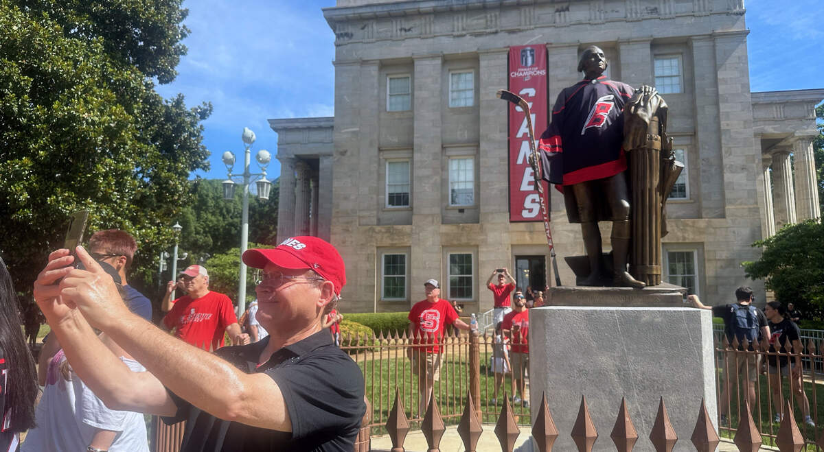Canes fans take selfies by the statue of George Washington decorated with Canes gear on the grounds of the State Capitol.