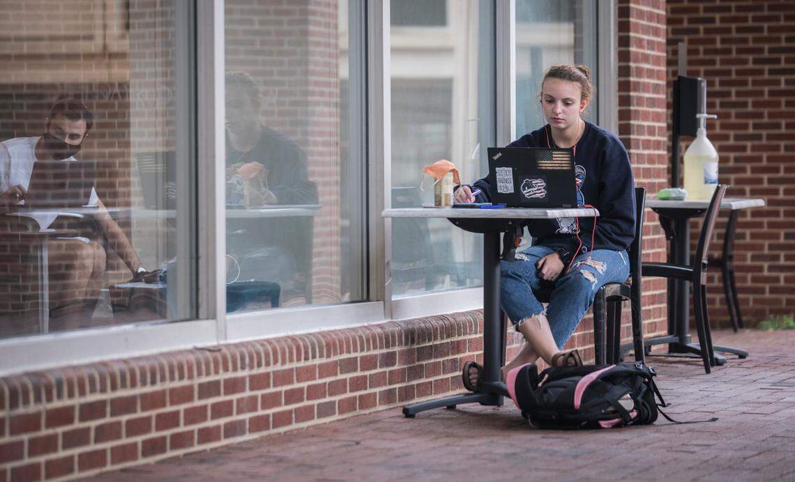 Kristen Snyder, a first year UNC student, attends an online class on her laptop outside of Davis Library in Chapel Hill, N.C. while another student works inside on Wednesday, Sept. 9, 2020.