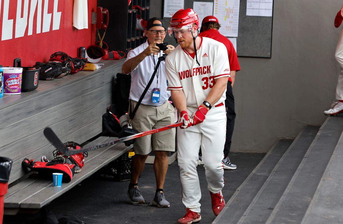 N.C. State’s Garrett Pennington (33) celebrates with a hockey helmet and stick in the dugout after hitting a two-run home run in the third inning during N.C. State’s game against South Carolina in the NCAA Raleigh Regional at Doak Field Saturday, June 1, 2024.