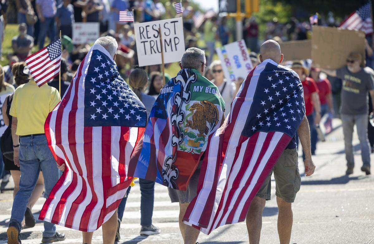 Demonstrators draped in flags cross Sumner Blvd. during the ‘No Kings’ rally along Capital Blvd. on Saturday, October 18, 2025 in Raleigh, N.C. 