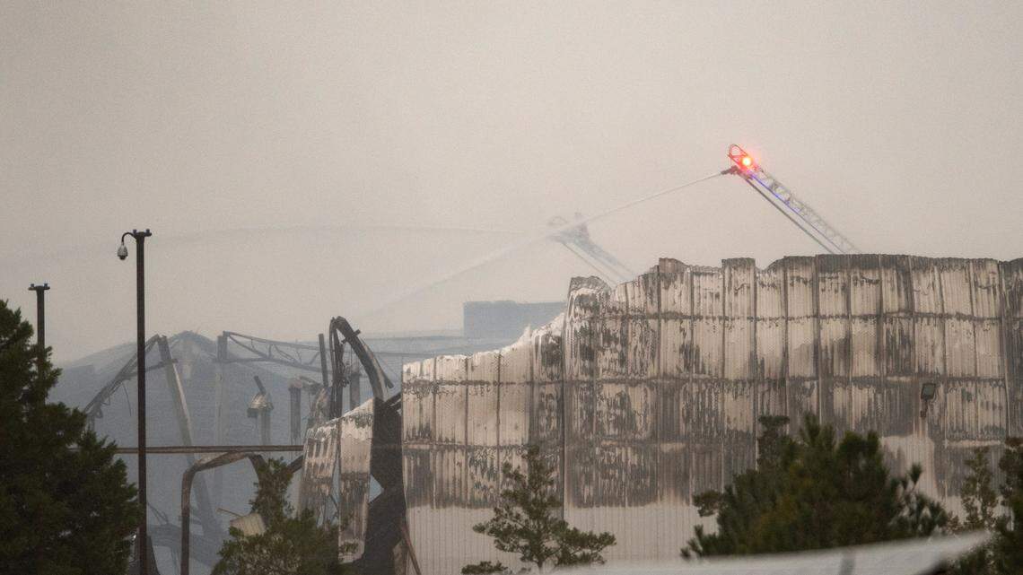 Aerial water cannons continue to spray water on sections of the QVC shipping facility in Rocky Mount, N.C. Sunday morning, Dec. 19. 2021 after a fire that started early Saturday morning gutted large sections of the building, collapsing the roof and parts of some walls.