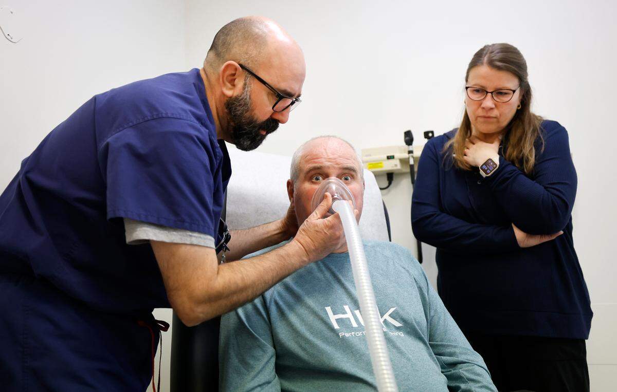 As Jamie Woodlief watches, Respiratory Therapist Mark Sollars helps fine tune the settings for a cough assist machine for Roy Woodlief during his appointment at the Duke ALS Clinic in Durham, N.C., Tuesday, Jan. 21, 2025. Roy has been diagnosed with amyotrophic lateral sclerosis (ALS), forcing him to retire from the Wake County Sheriff’s Office. The fatal disease causes muscle weakness, making it difficult to walk, eat and eventually breathe.