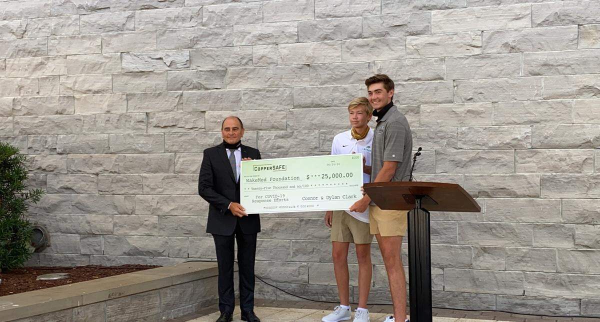 Donald R. Gintzig, President & CEO of WakeMed, receives a check for $25,000 from Dylan and Connor Clark. The Clark brothers started CopperSAFE, a copper-infused mask company, with the hopes of donating $100,000 to local hospitals.