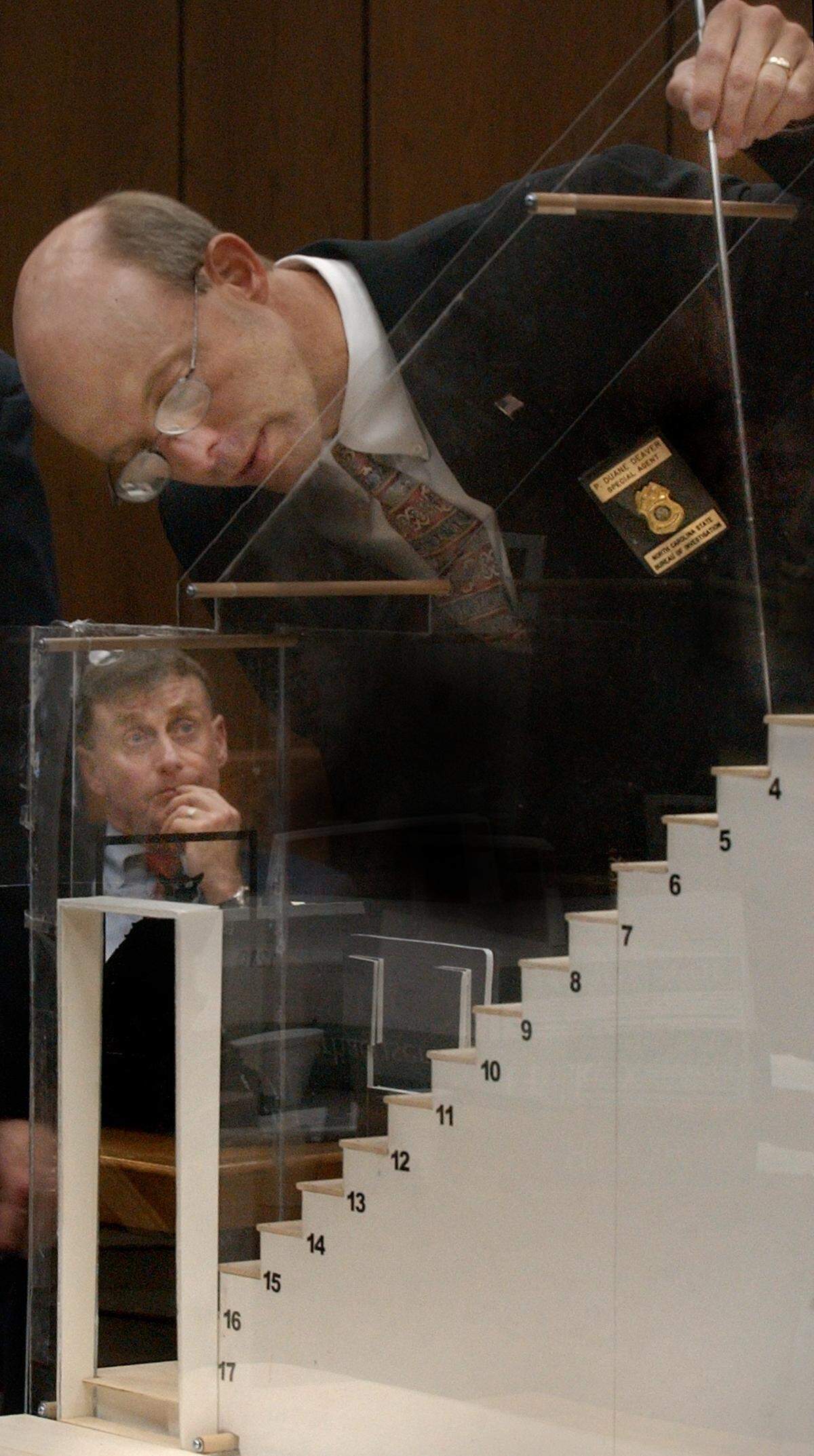 SBI blood spatter expert Duane Deaver uses a scale model of the Peterson stairway where he shows places he documented blood spatter on the steps where Kathleen Peterson was found dead in December 2001. Her husband Michael Peterson (at left) is accused of beating her to death and is on trial for her murder.