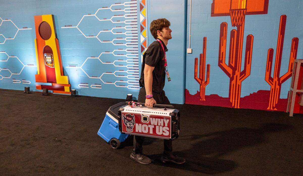 A manger for the Wolfpack basketball team leaves the locker room with the team’s gear including their their March Madness “Why not Us” boom box, following their season ending loss to Purdue on Saturday, April 6, 2024 at State Farm Stadium in Glendale, AZ.