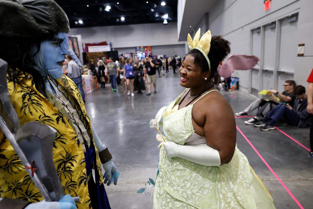 Vashti Parker of Eastover laughs with Jim Mooty of Winterville at GalaxyCon Raleigh at the Raleigh Convention Center Sunday, July 28, 2024. Parker is dressed as Princess Tianna from Princess and the Frog and Mooty is dressed as Arlong from One Piece.