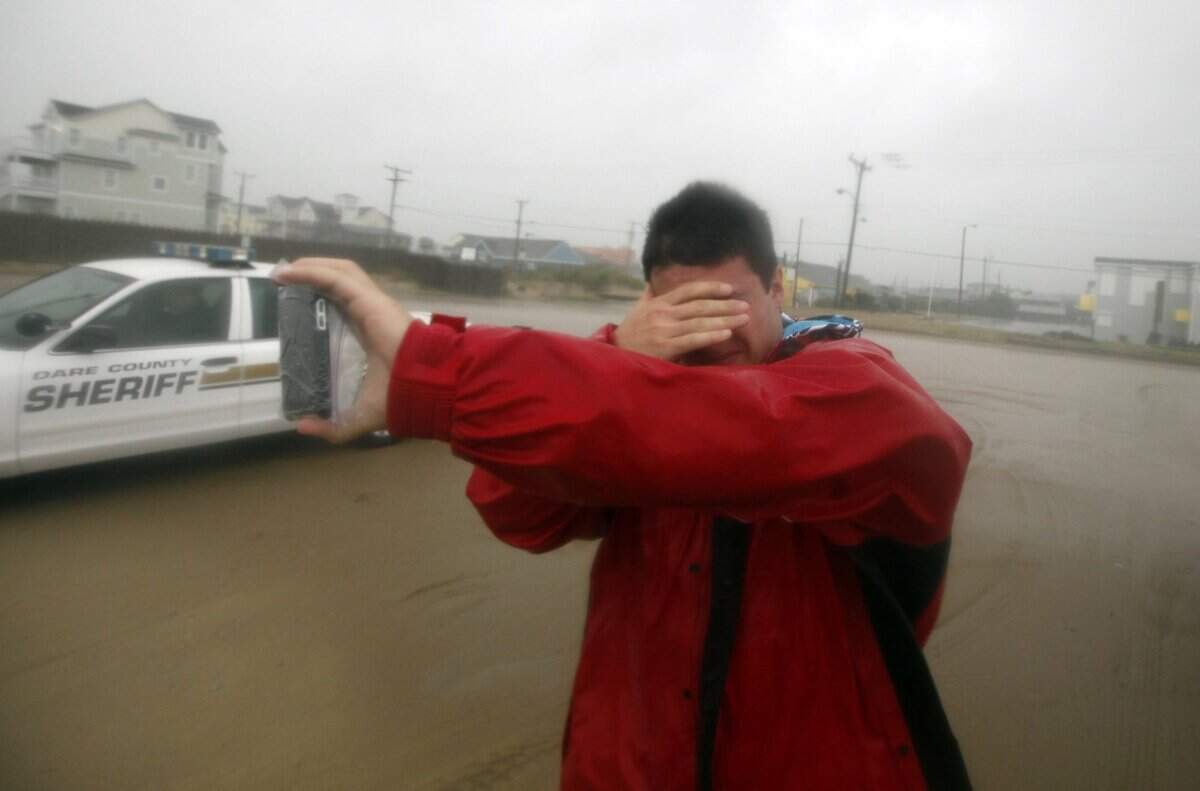 Shielding his eyes from the driving sand Mike Scruggs takes a photo of the beach at Avalon Pier in Kill Devil Hills during Hurricane Irene on Saturday, August 27, 2011.