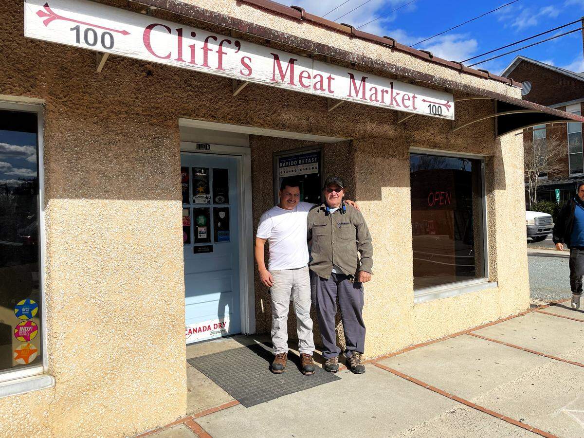 Owner Gerardo Martinez Galvan stands outside Cliff’s Meat Market in Carrboro with Cliff Collins, who established the butcher shop in 1973 and hired Martinez nearly 26 years ago. Martinez bought the store in 2020.