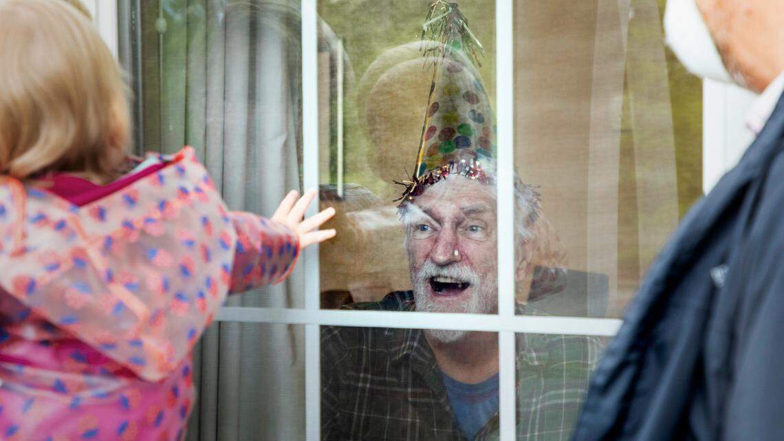 Jim Maxwell celebrates his 80th birthday through the window of his assisted living facility, The Addison of Durham, with his daughter Leslie Maxwell, left, and her husband and daughter, Steve and Brooks Gardner, on Saturday, Apr. 18, 2020, in Durham, N.C.