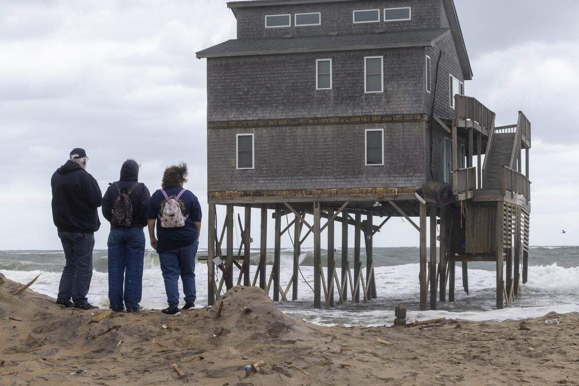 Beachgoers watch as rough surf threatens a beach home during high tide in Buxton on Friday.