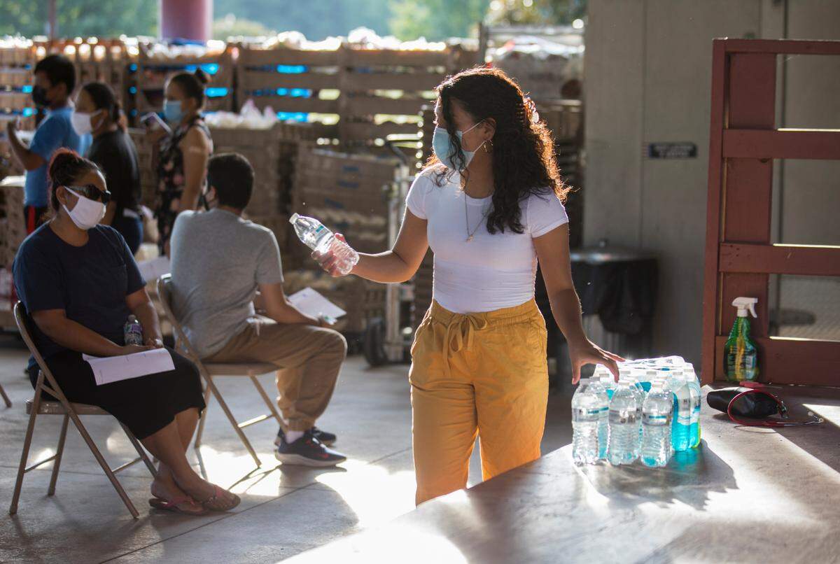 Karina Azuara, an interpreter volunteering at the Episcopal Farm Worker Ministry vaccine clinic in Dunn, N.C., passes out water bottles as people sit and wait after receiving the COVID-19 vaccine on Sept. 4, 2021.