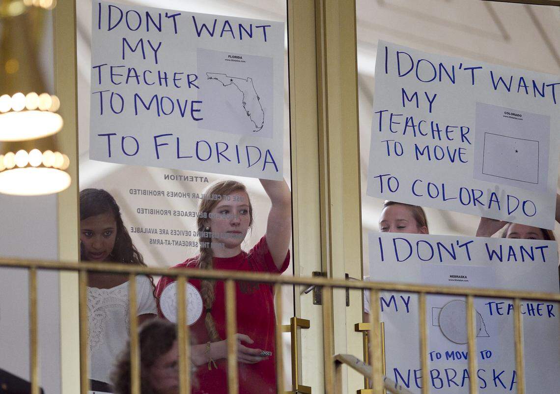 Student protestors hold their protest signs calling for better teacher pay against the glass of the State House Chamber's second floor during a 2014 protest.