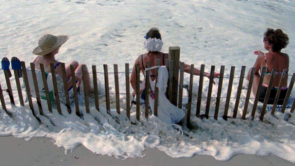 Vacationers sit along the edge of  the surf along Indian Beach.