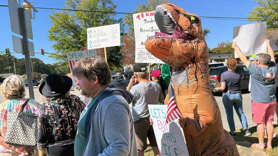 No Kings protesters, including one in a dinosaur costume, march along Kildare Farm Road in Cary, Saturday, October 18, 2025.