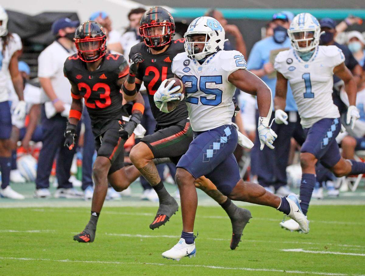 North Carolina Tar Heels running back Javonte Williams (25) runs the ball in the second quarter as University of Miami cornerback Te’Cory Couch (23) and Bubba Bolden (21) give chase at Hard Rock Stadium In Miami Gardens, Florida, Saturday, December 12, 2020.