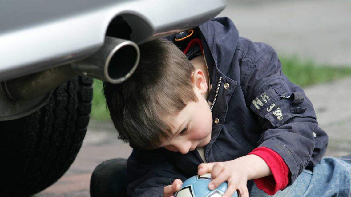In this photo, five years old Anton Tietze plays with his ball near the exhaust pipe of a car in Bremen, northern Germany, Wednesday, March 30 2005. Half of American adults have shrunken IQ scores due to lead exposure from leaded gasoline from car exhaust as children, a study found. Millions are affected.