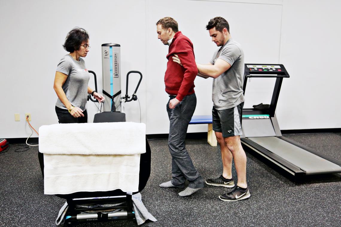 Next Step Raleigh director of training Arlene Peters, left, and activity based trainer David Wright, right, work with Mike Thor to stand up and take steps during one of his therapy sessions at Next Step Raleigh on Dec. 6, 2018. Thor is determined to walk again and pushes himself through multiple therapy sessions a week.